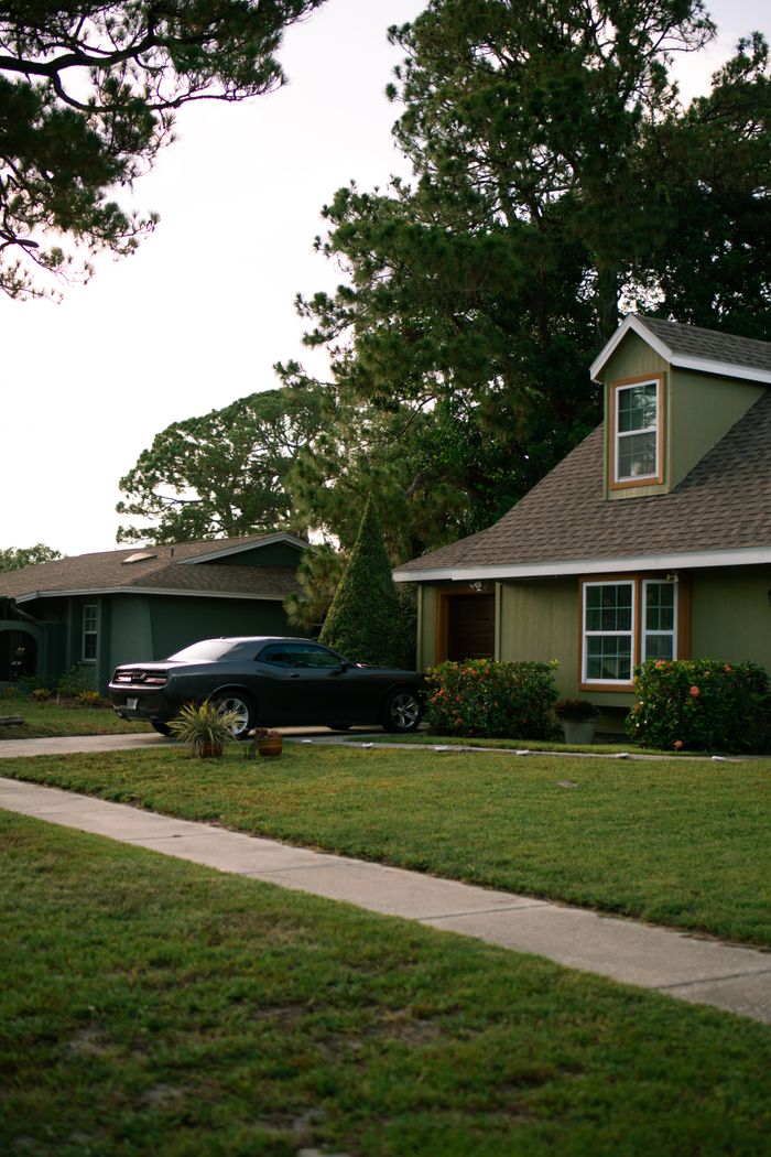 hero-img-01 Charming suburban house with well-maintained lawn and car in driveway at dusk, featuring lush trees and peaceful setting.