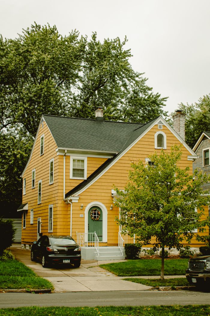 ours-journey A charming yellow two-story house with a green door, car parked outside.