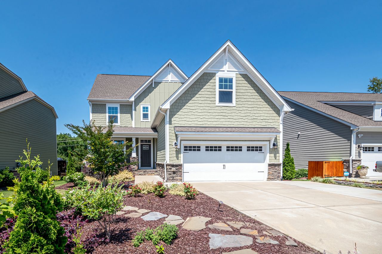 Mastering the First Impression: Your intriguing post title goes here Charming suburban house with green facade, garage, and landscaped yard on a clear day.