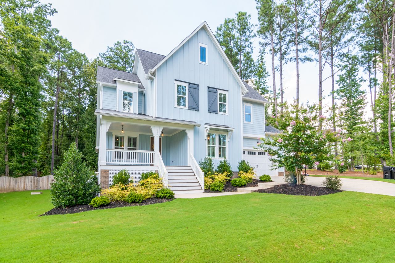 services-02 Elegant light blue suburban home with a lush lawn and forest backdrop.